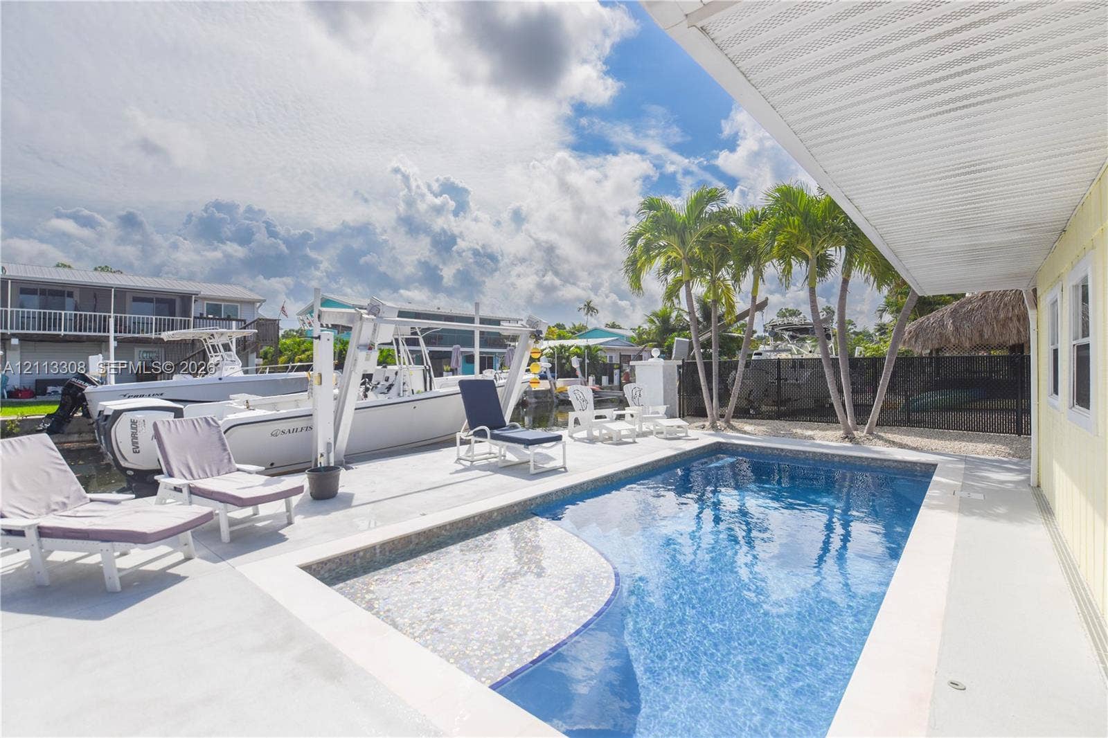Concrete pool deck featuring an in-ground swimming pool, private boat lift, and canal bulkhead access