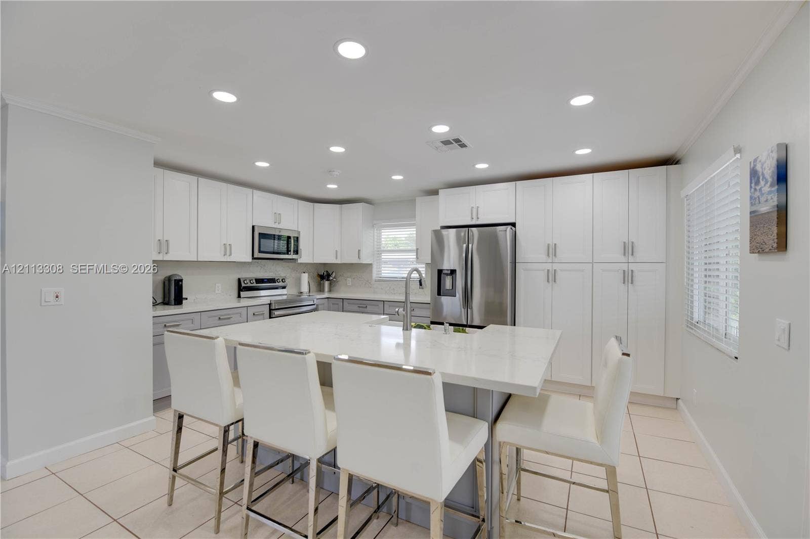 Kitchen featuring white cabinetry, an expansive central island with quartz countertops, stainless steel appliances, recessed ceiling lighting, and ceramic tile flooring