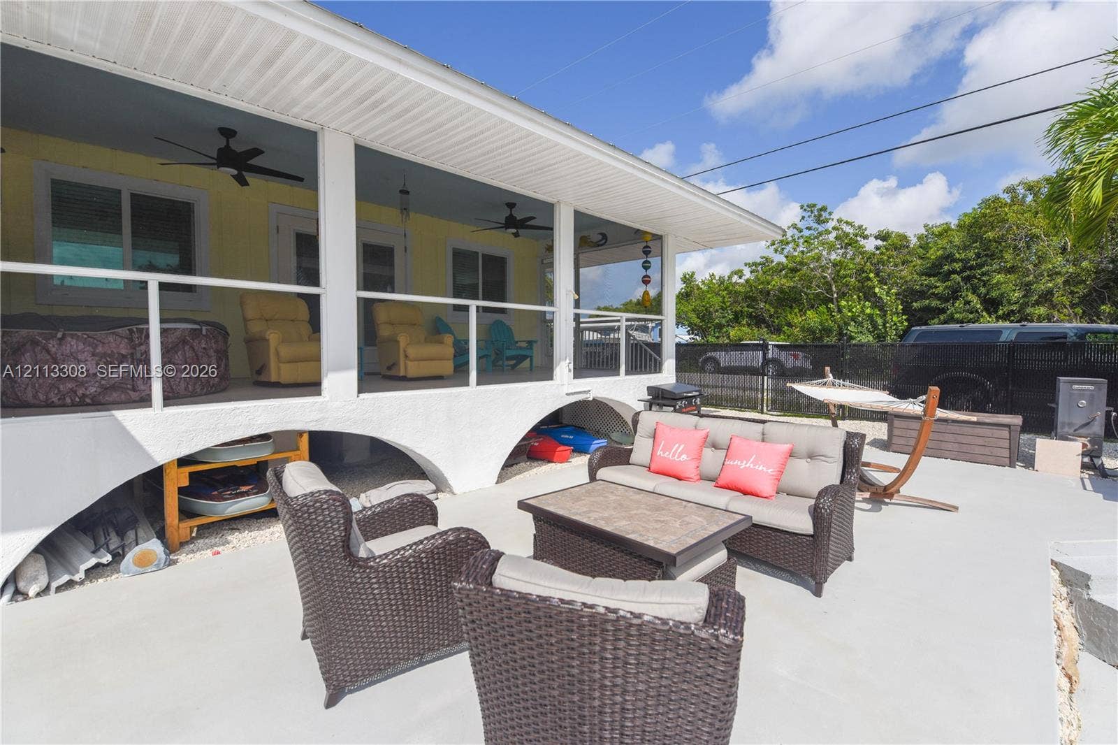 Screened-in porch featuring white structural columns, arched concrete foundation, dual ceiling fans, and a concrete patio space