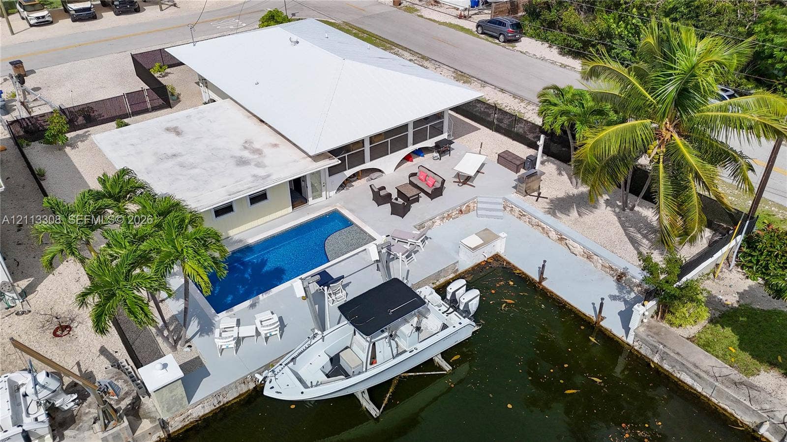 Waterfront residence featuring a private swimming pool, concrete boat slip with lift, expansive paved patio, and mature palm trees