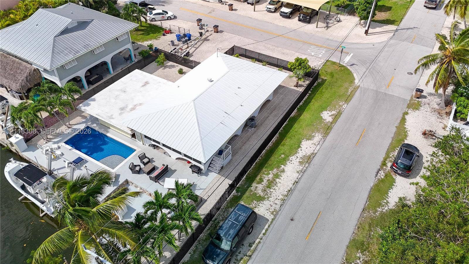 Aerial perspective of a waterfront property featuring a concrete pool deck, in-ground swimming pool, metal roof, and direct bulkhead boat docking