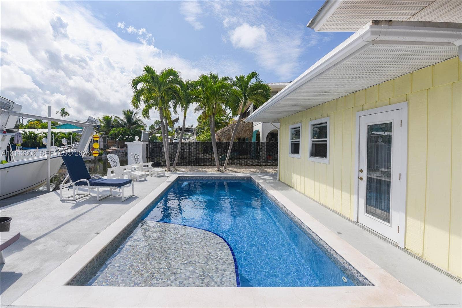 Rectangular swimming pool with integrated tanning ledge, light-toned vertical siding, concrete pool deck, and water-level bulkhead
