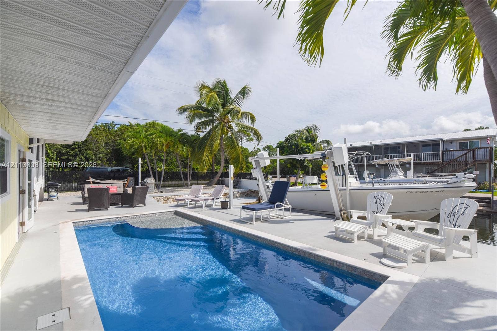 In-ground swimming pool featuring a tiled perimeter, expansive concrete deck, built-in boat lift, and bulkhead docking