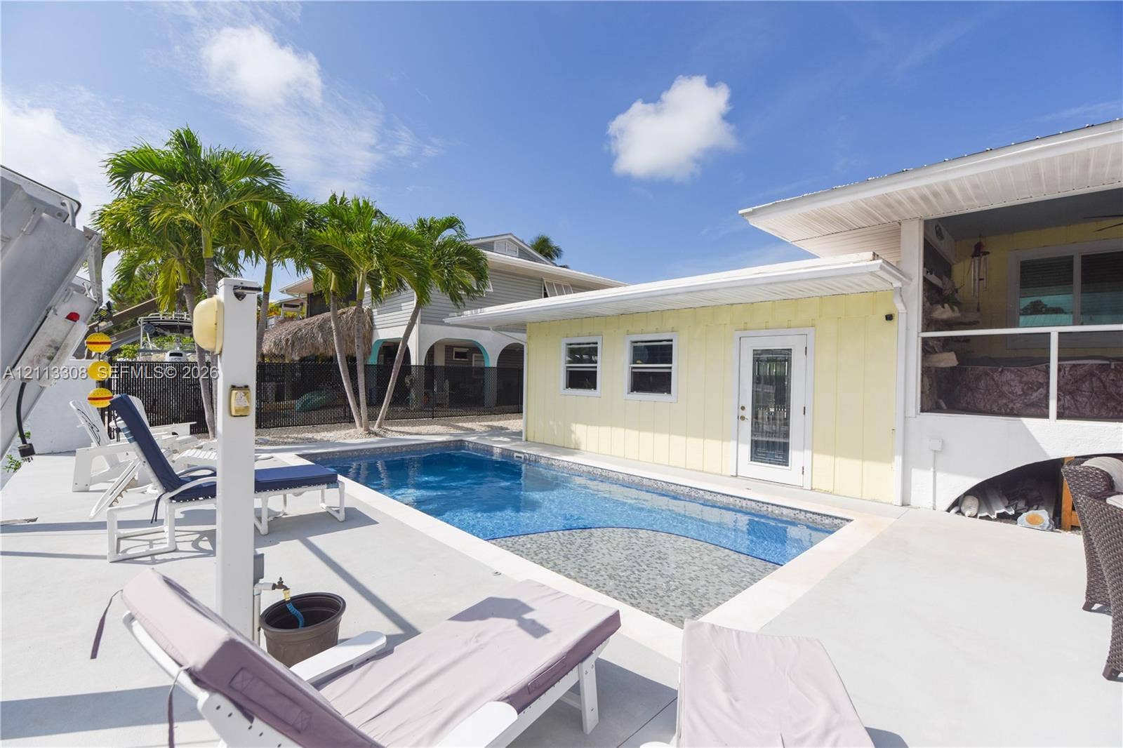 In-ground swimming pool with tiled interior, expansive concrete deck, yellow siding exterior, and palm trees