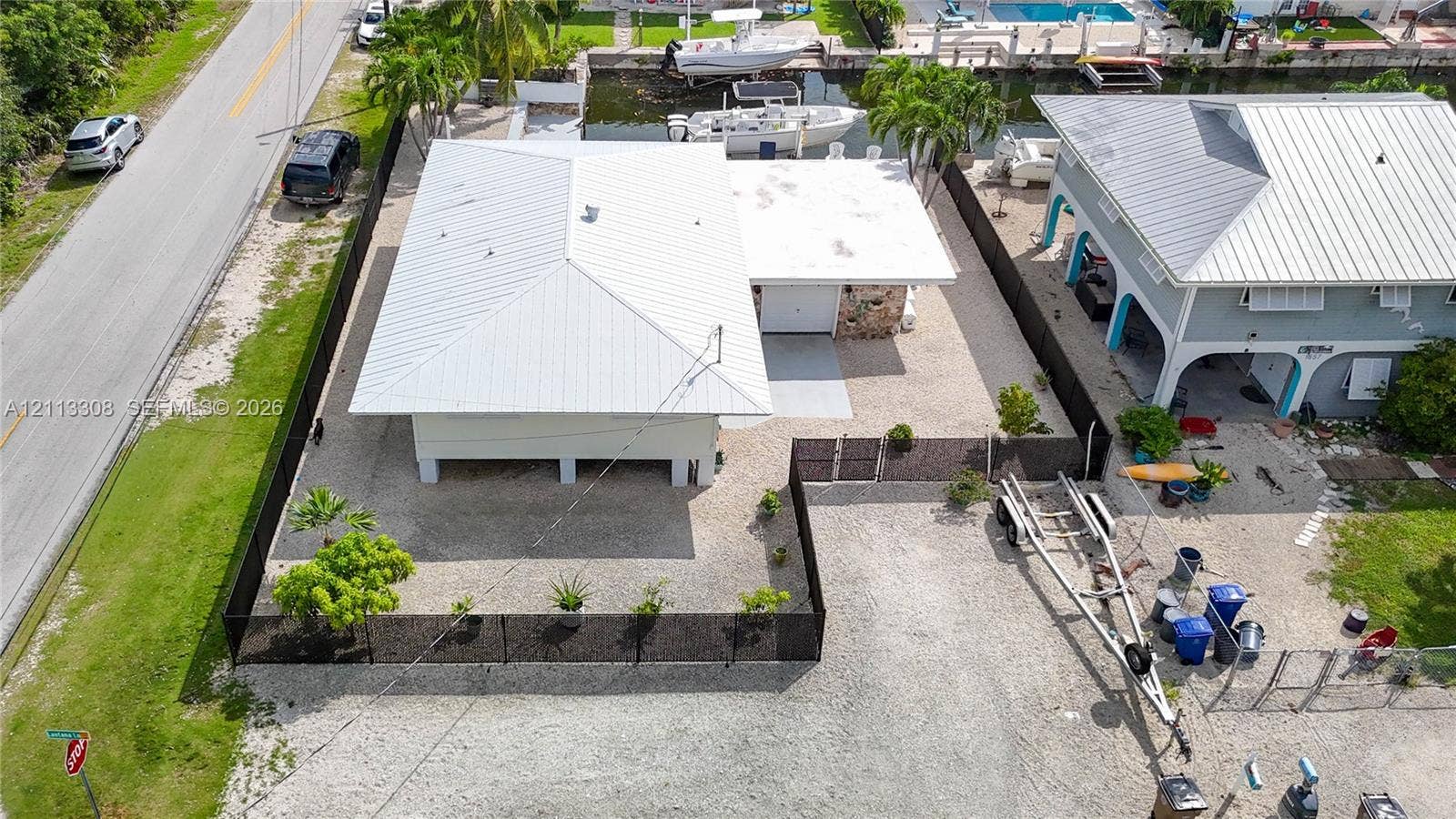 Aerial view of a waterfront property featuring a metal roof, elevated structure, stone masonry detailing, and perimeter fencing