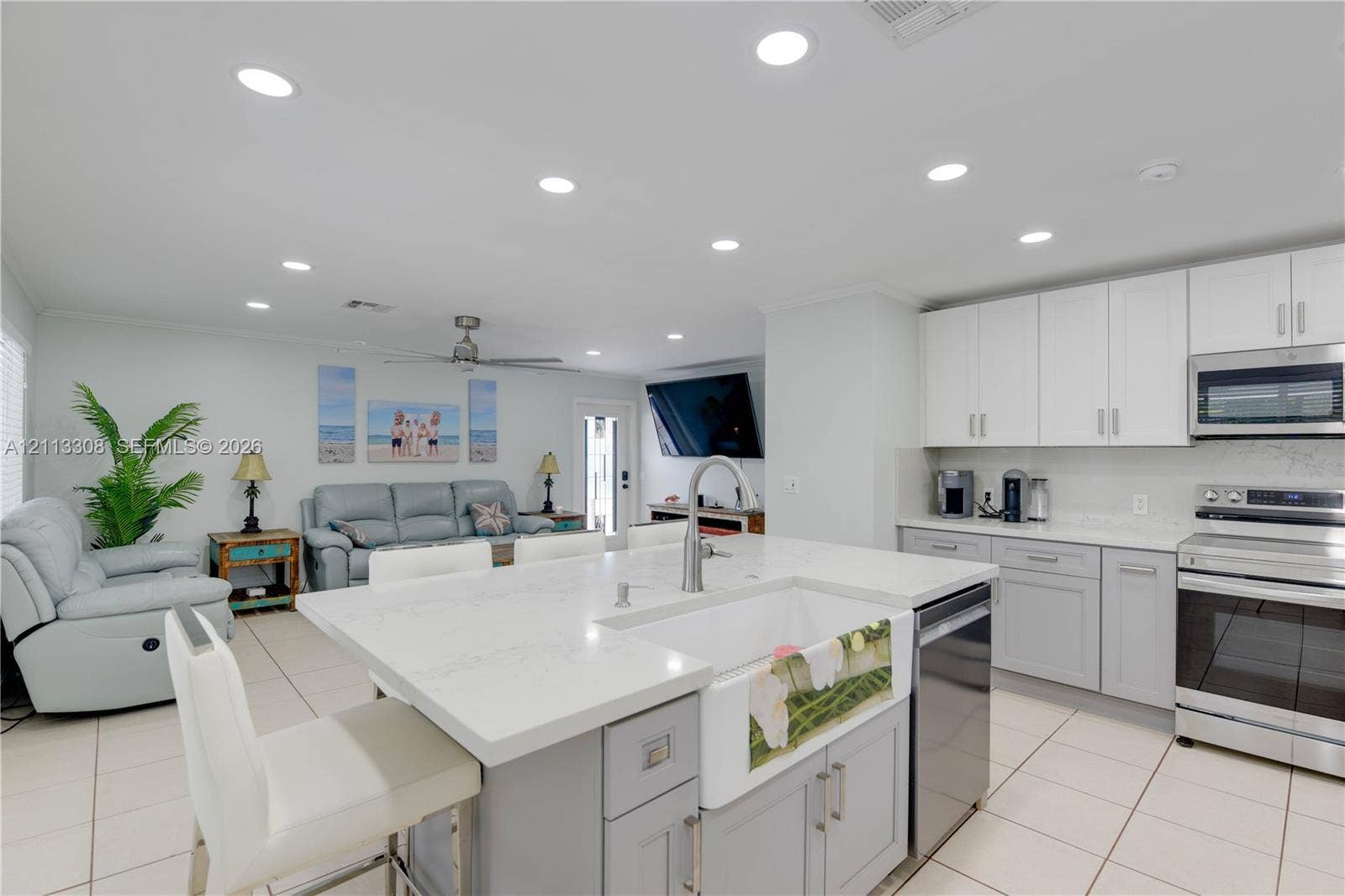 Kitchen featuring a central island with a farmhouse-style apron sink, quartz countertops, white shaker-style cabinetry, stainless steel appliances, and tile flooring