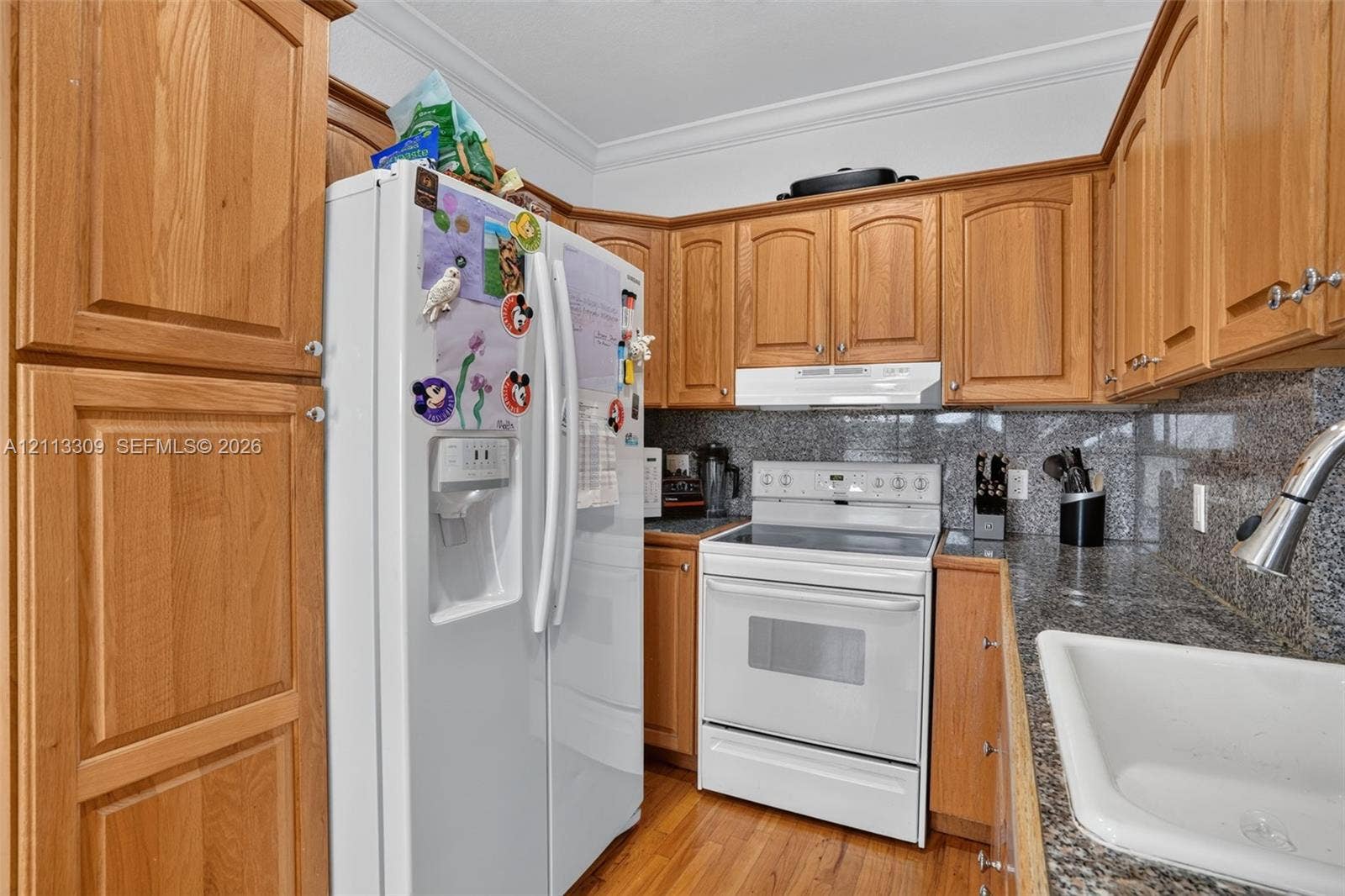 3082 Bird Avenue, #6, Miami, FL 33133 Kitchen featuring wood cabinetry, stone-finish countertops, crown molding, white appliance suite, and a white drop-in sink with a pull-down faucet