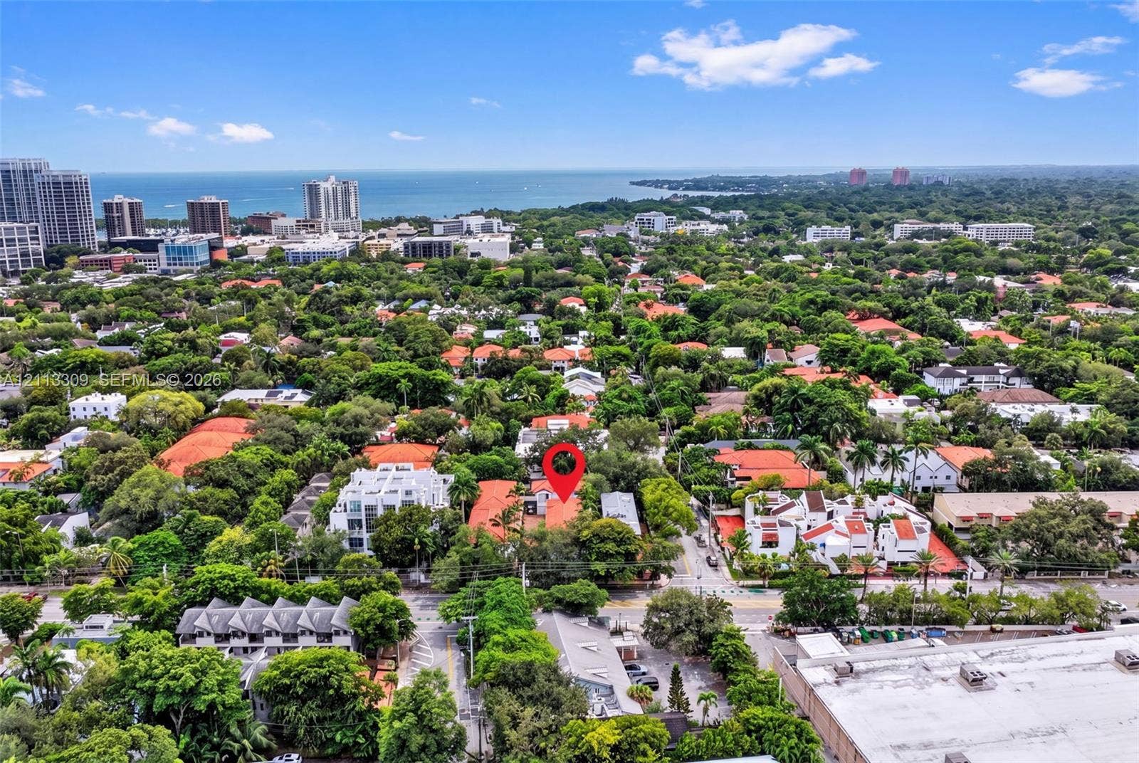 3082 Bird Avenue, #6, Miami, FL 33133 Aerial perspective featuring a red-tile roof structure situated within a densely wooded suburban setting, including prominent coastal and horizon scenery