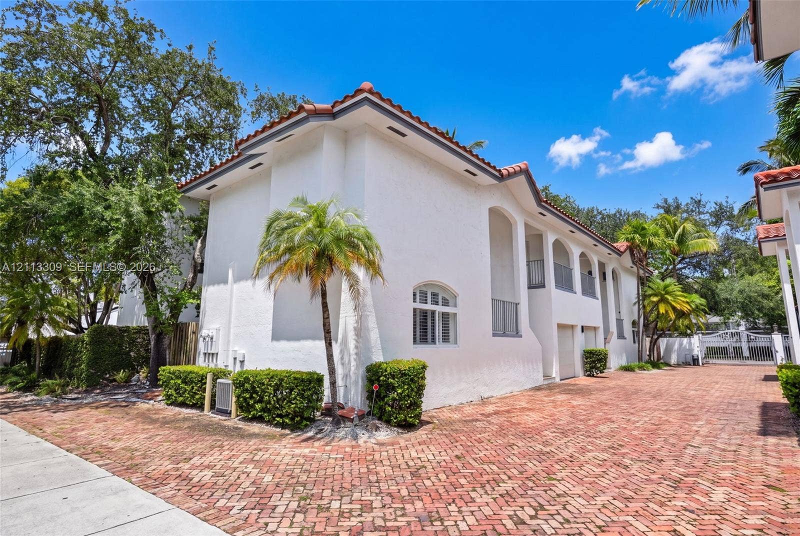 3082 Bird Avenue, #6, Miami, FL 33133 Stucco exterior featuring arched architectural detailing, a clay tile roof, second-story balconies, and a red brick driveway
