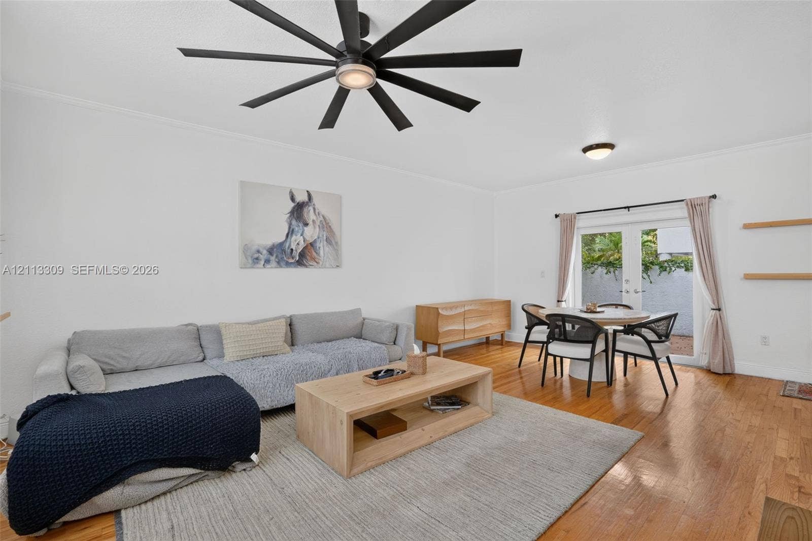 3082 Bird Avenue, #6, Miami, FL 33133 Interior space featuring wood-finish flooring, a contemporary multi-blade ceiling fan, glass-paned double doors, and wall-mounted floating shelves