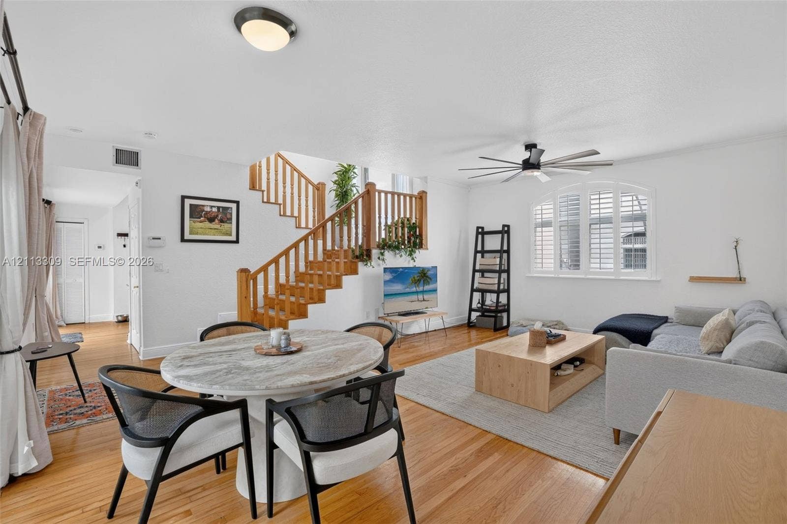 3082 Bird Avenue, #6, Miami, FL 33133 Open floor plan featuring wood-finish flooring, a central staircase with wood railings, and a multi-pane arched window with plantation shutters