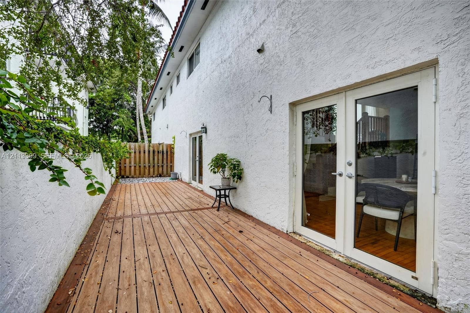 3082 Bird Avenue, #6, Miami, FL 33133 Exterior wood-finish decking featuring dual glass-paned double doors, white textured stucco walls, and a perimeter wood fence
