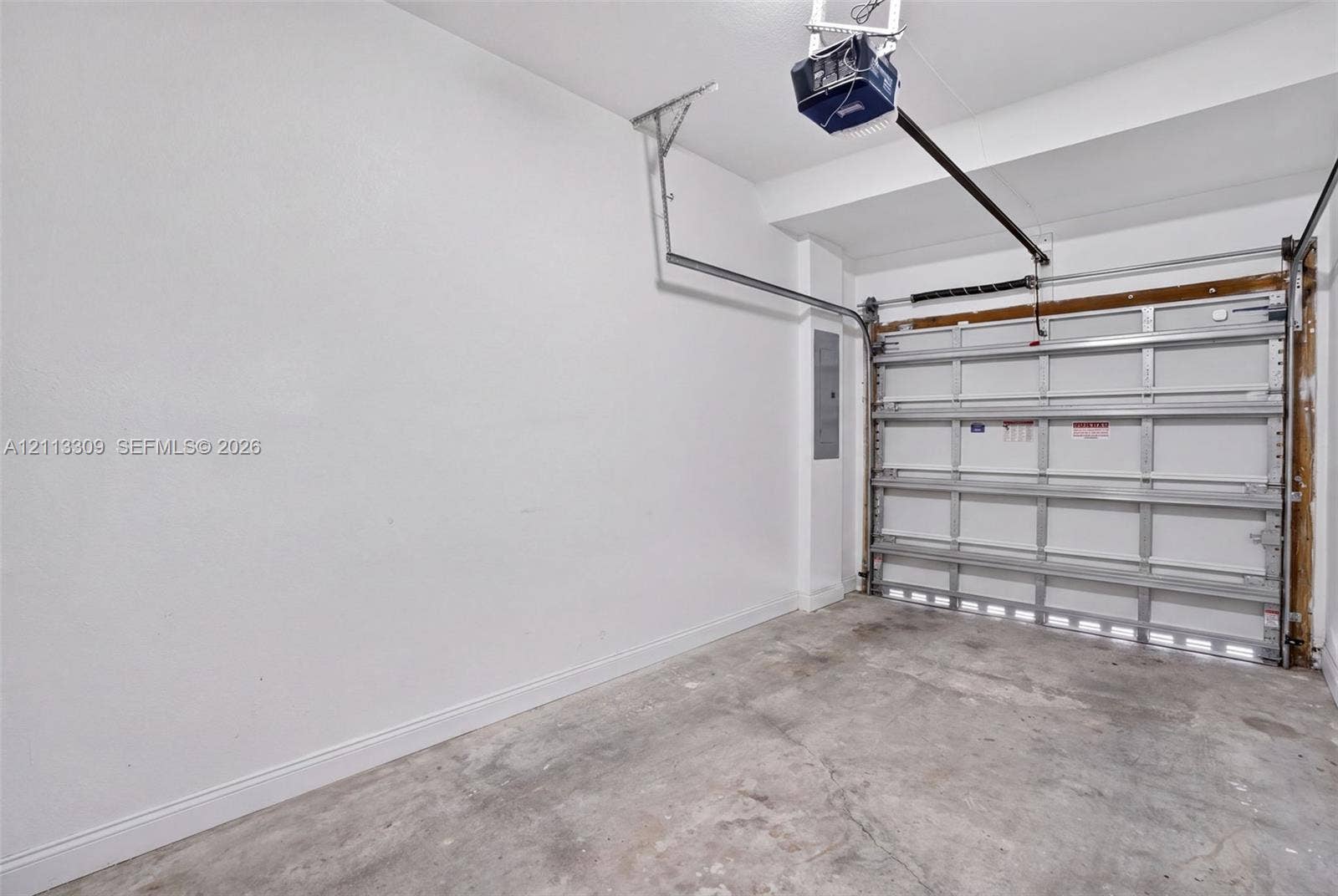 3082 Bird Avenue, #6, Miami, FL 33133 Garage interior featuring white finished walls, concrete flooring, a paneled overhead door, and an integrated automatic garage door opener
