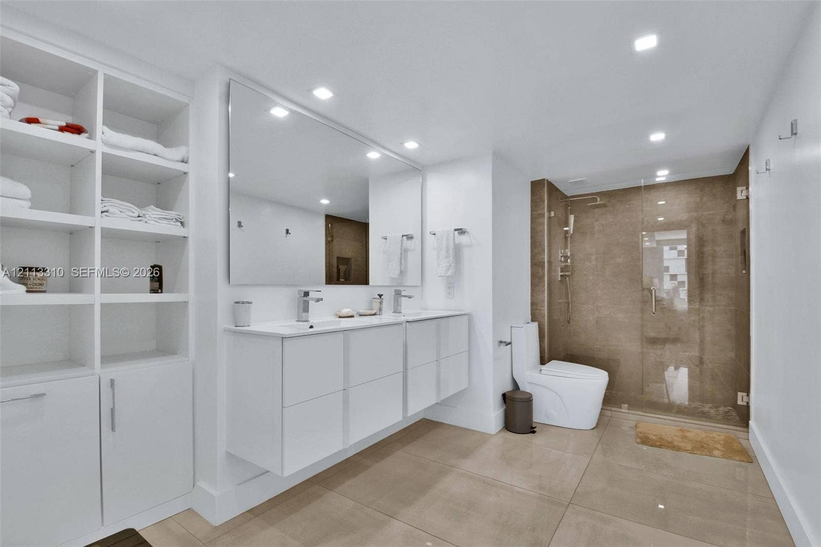 Bathroom featuring a floating double vanity with rectangular sinks, a floor-to-ceiling white built-in storage cabinet, large-format tile flooring, and a walk-in shower with a glass enclosure and tiled walls