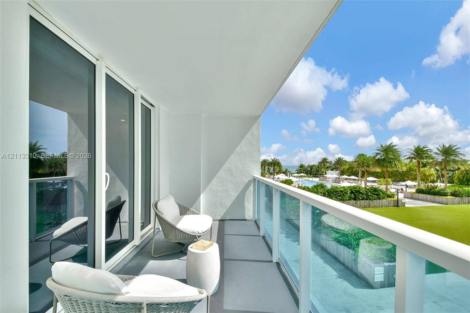 Covered balcony with a glass panel railing, sliding glass doors, and concrete flooring