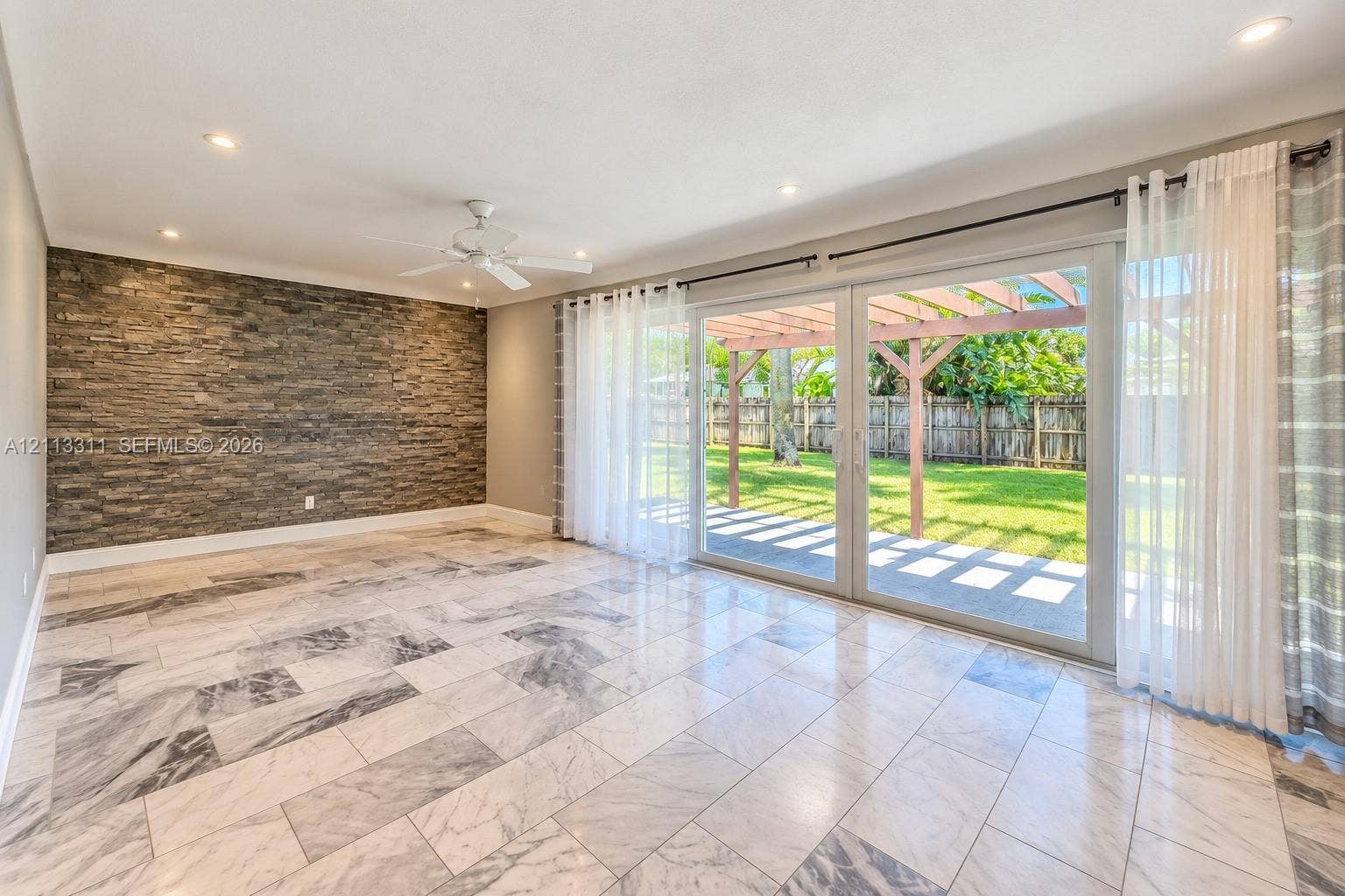 152 SW 59th Avenue, Plantation, Plantation, FL 33317 Stone veneer accent wall, large-format tile flooring, recessed lighting, and sliding glass doors opening to a covered patio with a wooden pergola