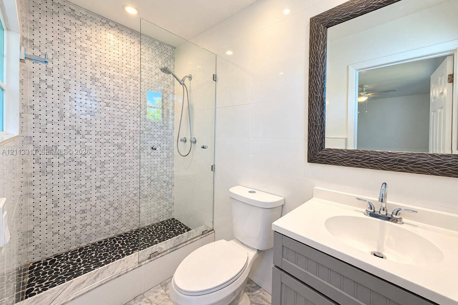 152 SW 59th Avenue, Plantation, Plantation, FL 33317 Walk-in shower featuring a frameless glass enclosure, decorative mosaic wall tile, and natural stone pebble flooring, complemented by a grey shaker-style vanity with a solid surface countertop