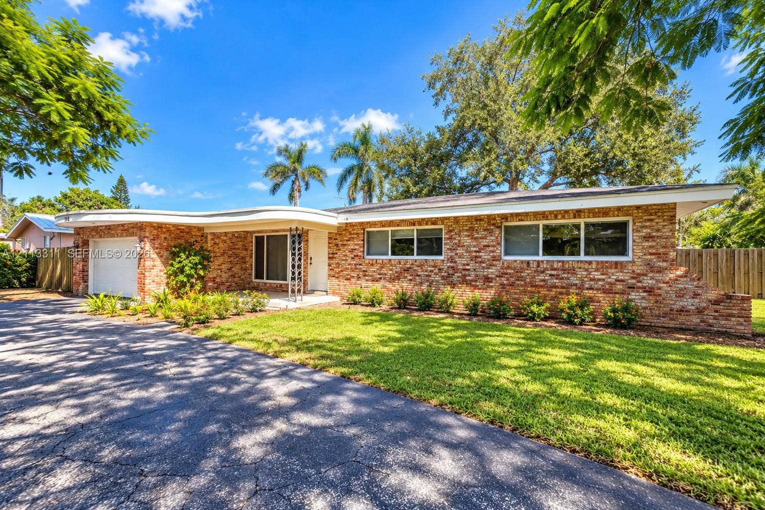 152 SW 59th Avenue, Plantation, Plantation, FL 33317 Single-story brick exterior featuring a distinctive curved roofline, an attached garage, a paved driveway, and mature landscaping