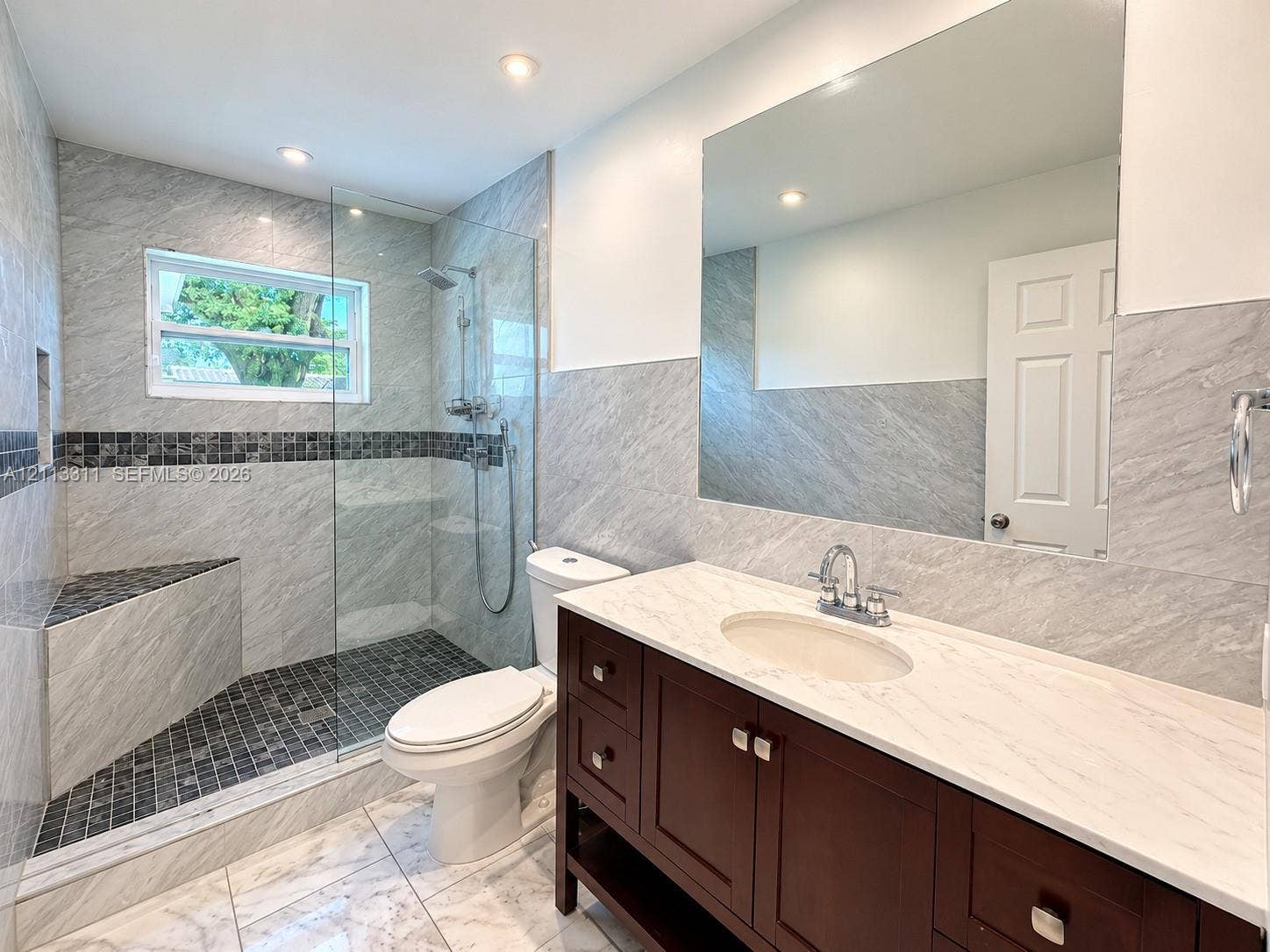 152 SW 59th Avenue, Plantation, Plantation, FL 33317 Bathroom featuring a wood-finish vanity with a light-toned countertop, a walk-in shower with a glass panel and built-in bench, recessed lighting, and large-format wall tiling with a mosaic accent border