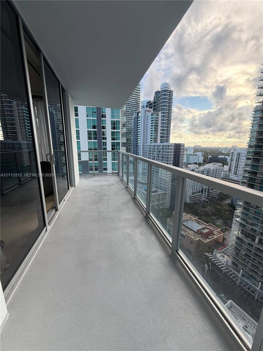 Covered outdoor balcony featuring a concrete floor, glass railings, and expansive cityscape horizons