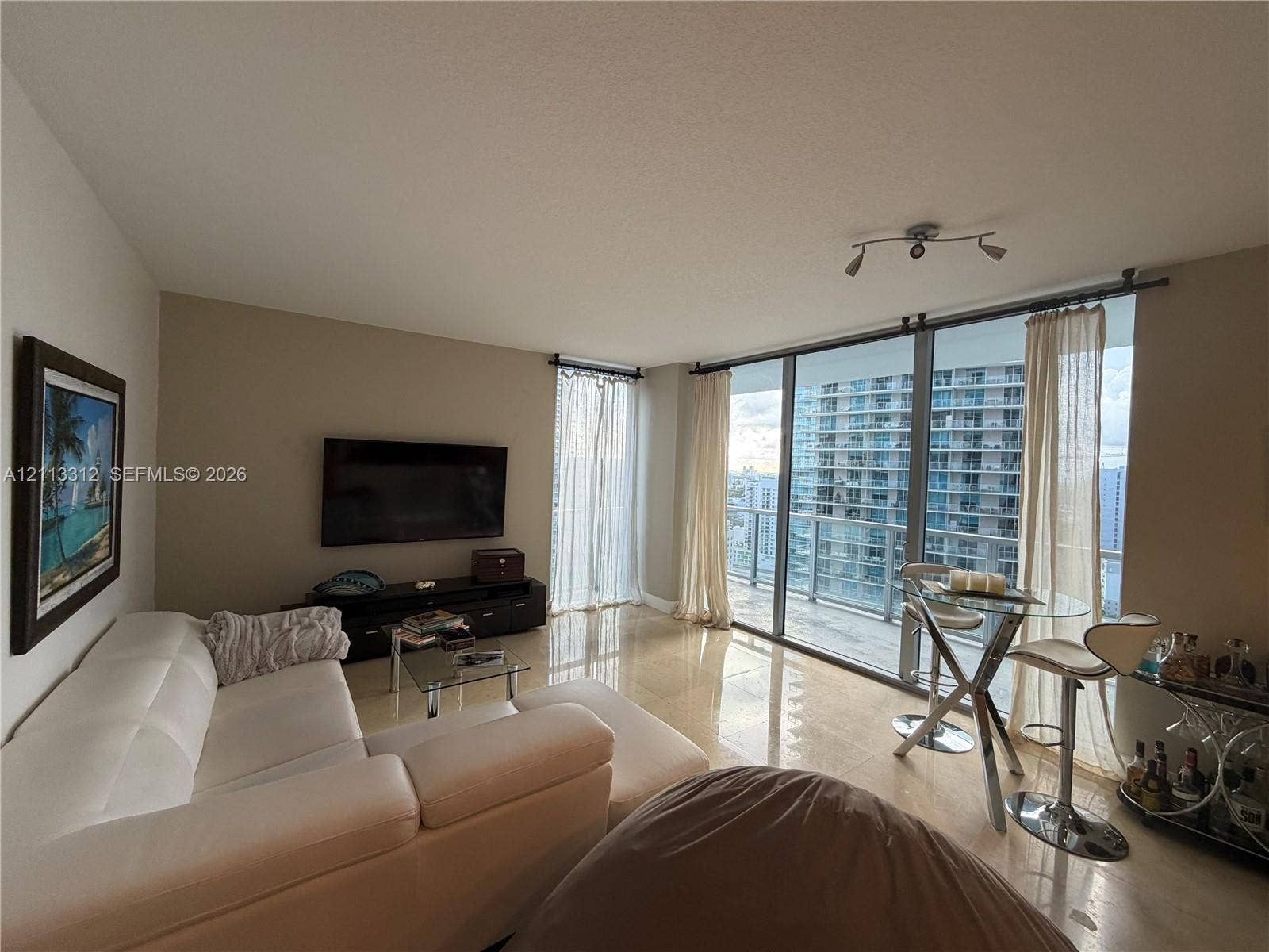 Floor-to-ceiling glass wall, polished tile flooring, integrated balcony access, and track lighting