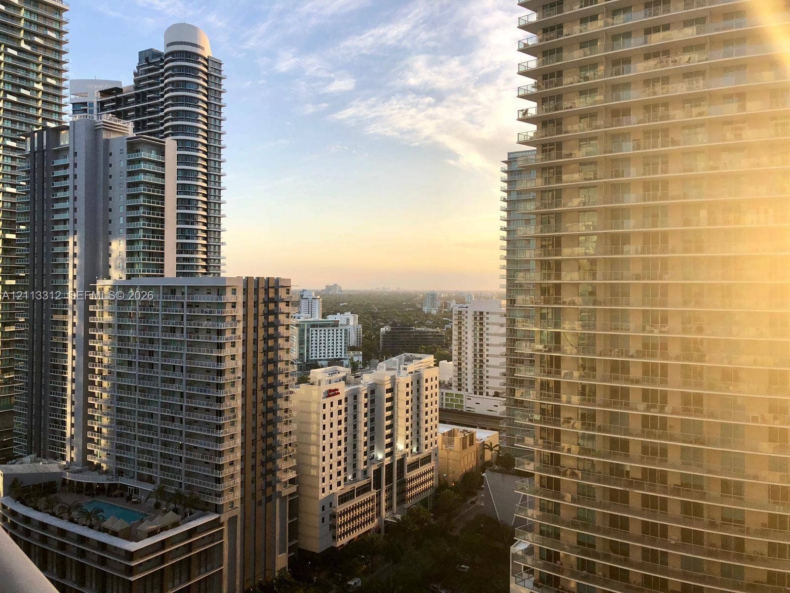 High-rise urban landscape featuring glass balcony railings, floor-to-ceiling windows, tiered building architecture, and an elevated outdoor swimming pool