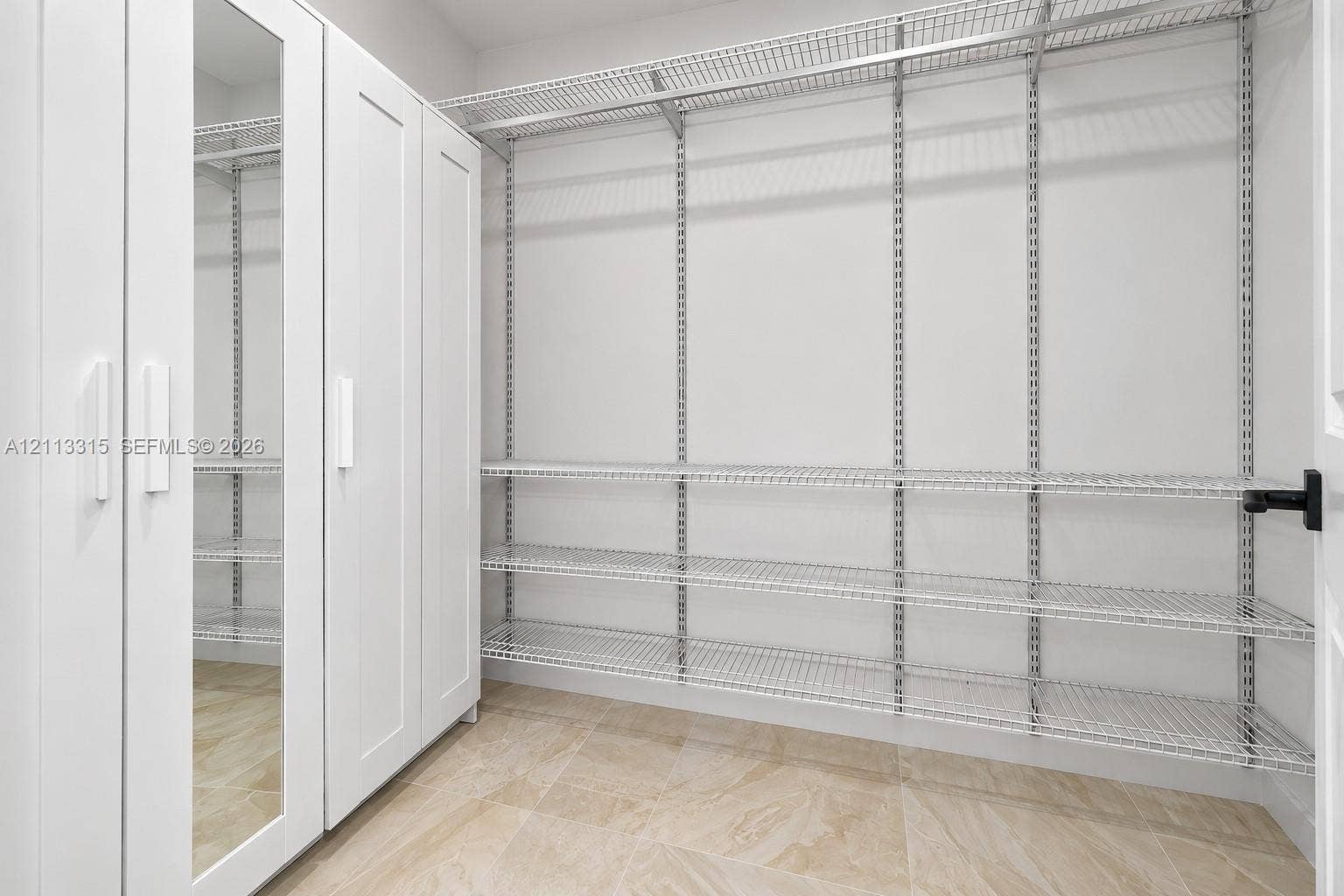 Storage area featuring floor-to-ceiling white cabinetry with a mirrored panel, multi-tier wire shelving, and stone-finish tile flooring