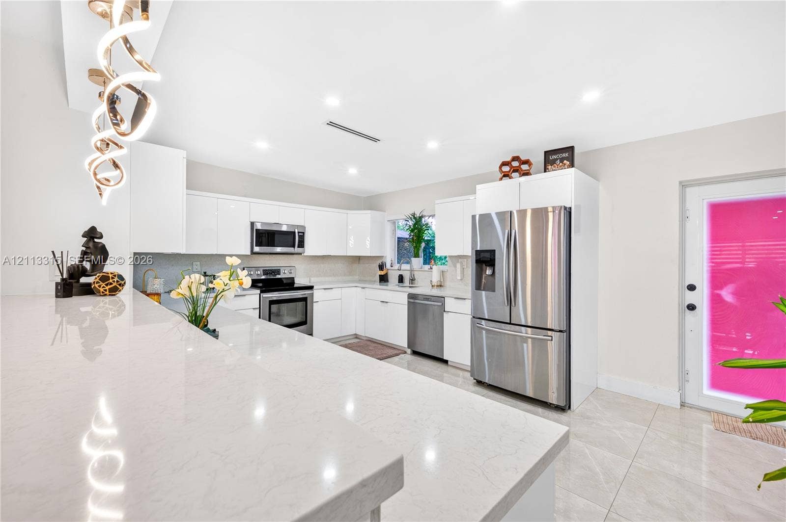 Kitchen featuring white slab-front cabinetry, quartz countertops, stainless steel appliances, large-format tile flooring, and a decorative spiral chandelier
