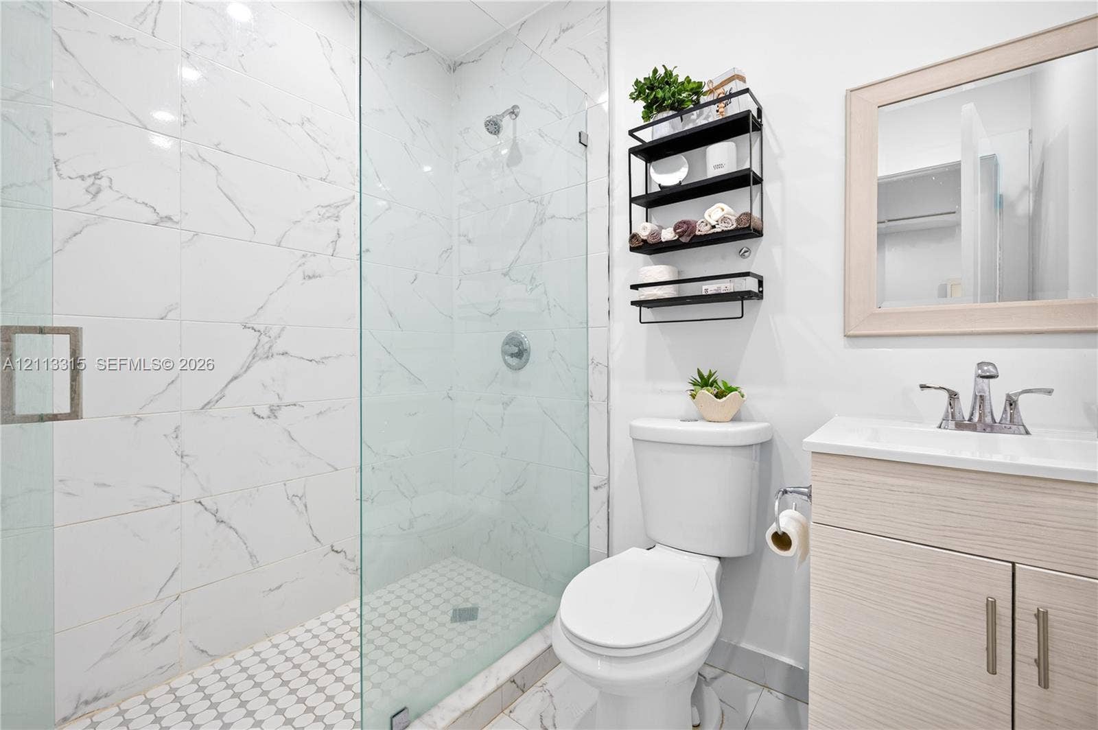 Walk-in shower with floor-to-ceiling large-format tile, glass enclosure, and circular mosaic tile flooring