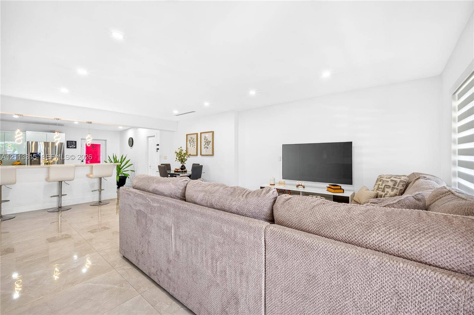 Open-concept interior featuring large-format polished tile flooring, recessed ceiling lighting, a breakfast bar with stone-finish surfacing, and horizontal window blinds
