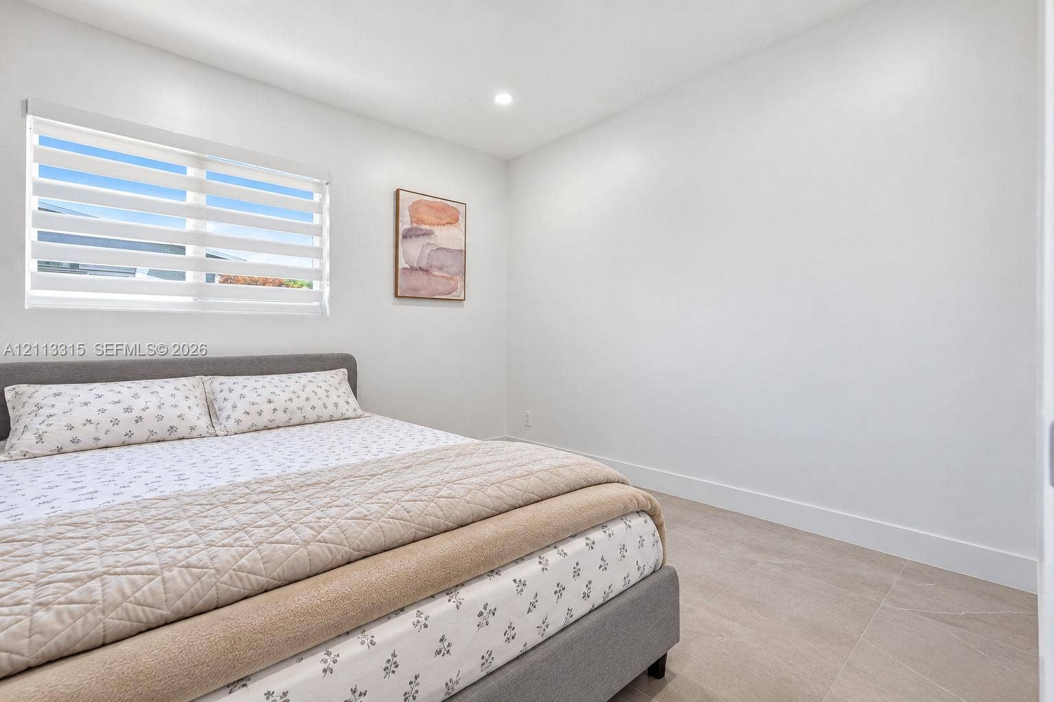 Neutral-toned room featuring large-format tile flooring, recessed ceiling lighting, and a window equipped with horizontal zebra-style shades