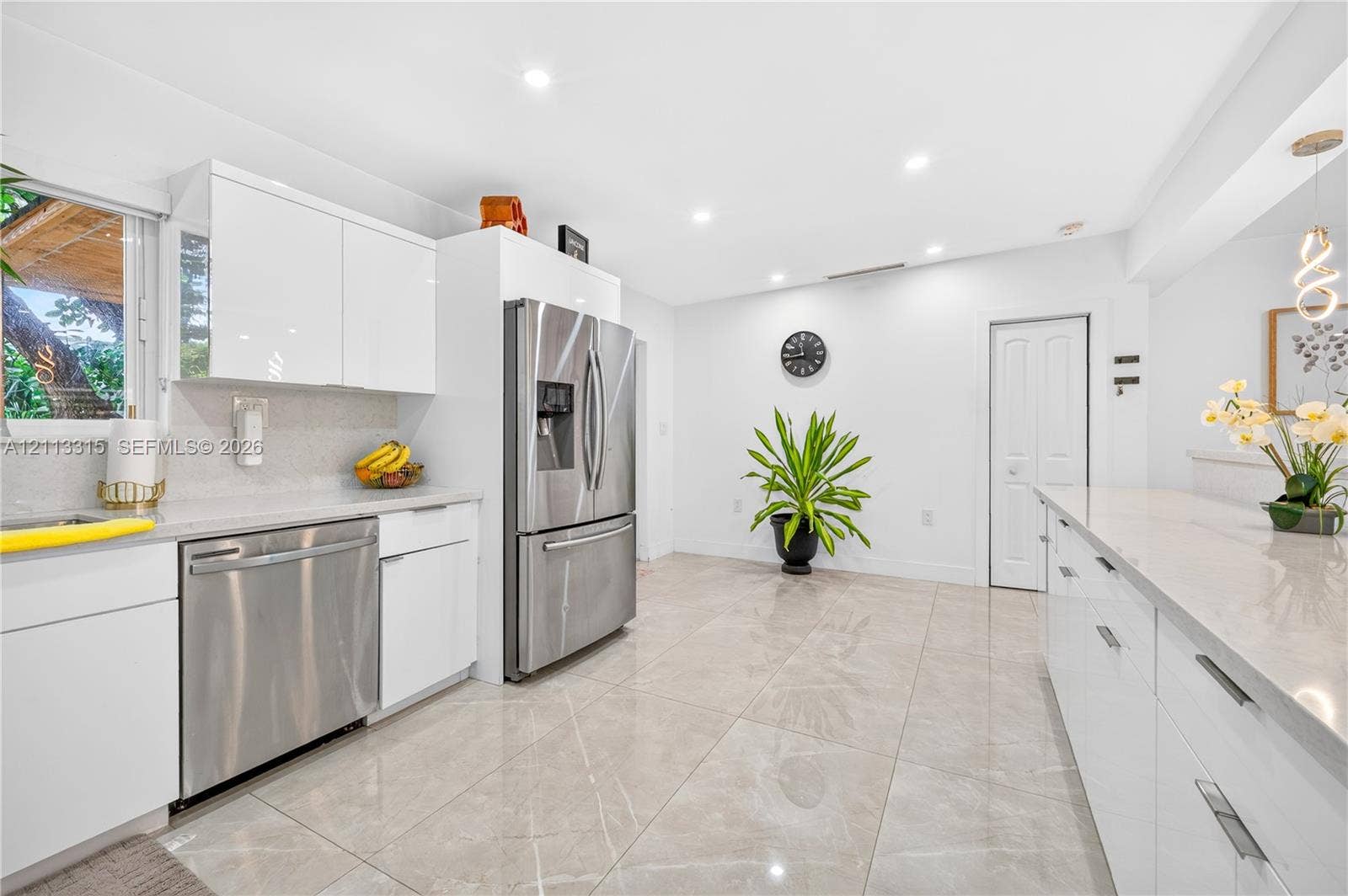 Kitchen featuring high-gloss white cabinetry, stainless steel appliances, expansive stone-finish countertops, and large-format porcelain tile flooring