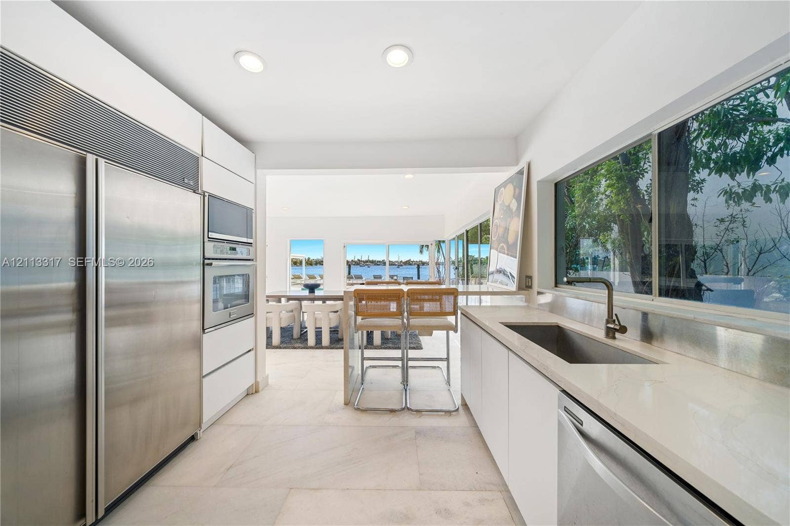 Kitchen featuring custom flat-panel cabinetry, professional-grade stainless steel appliances, stone countertops, integrated sink, and large-format tile flooring