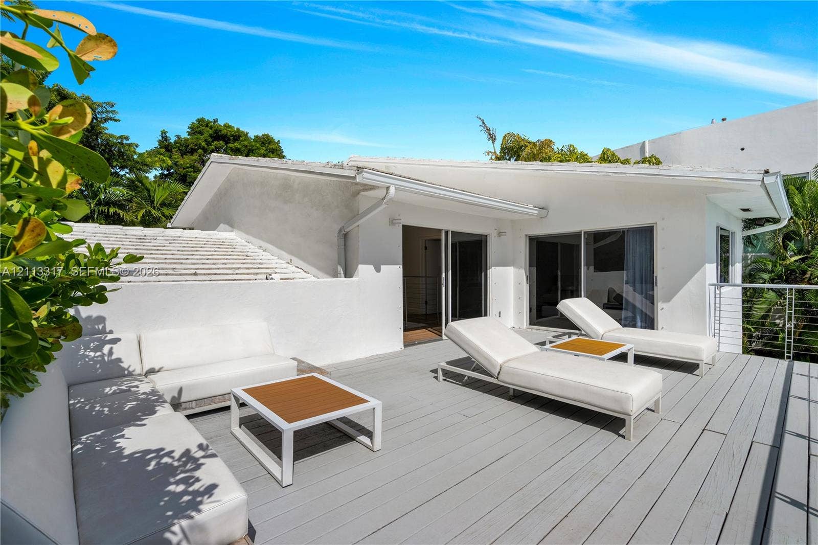 Elevated outdoor terrace featuring gray wood-finish decking, integrated built-in seating, glass sliding door entryways, and metal cable railing