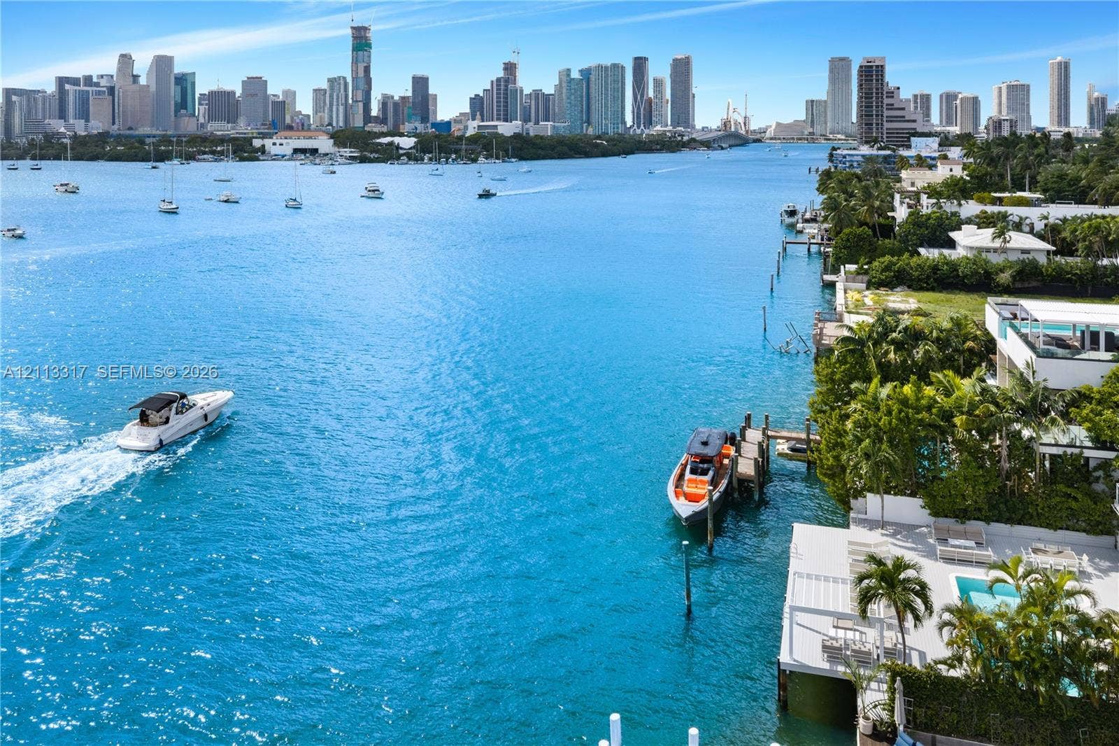 Waterfront property featuring a private boat dock, swimming pool, concrete patio, and direct waterway access with a backdrop of the city skyline