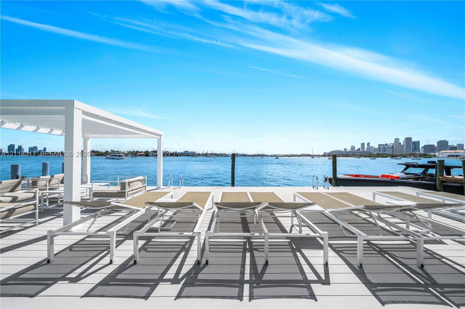 Waterfront dock featuring light-toned decking, a white pergola, and integrated marine pilings