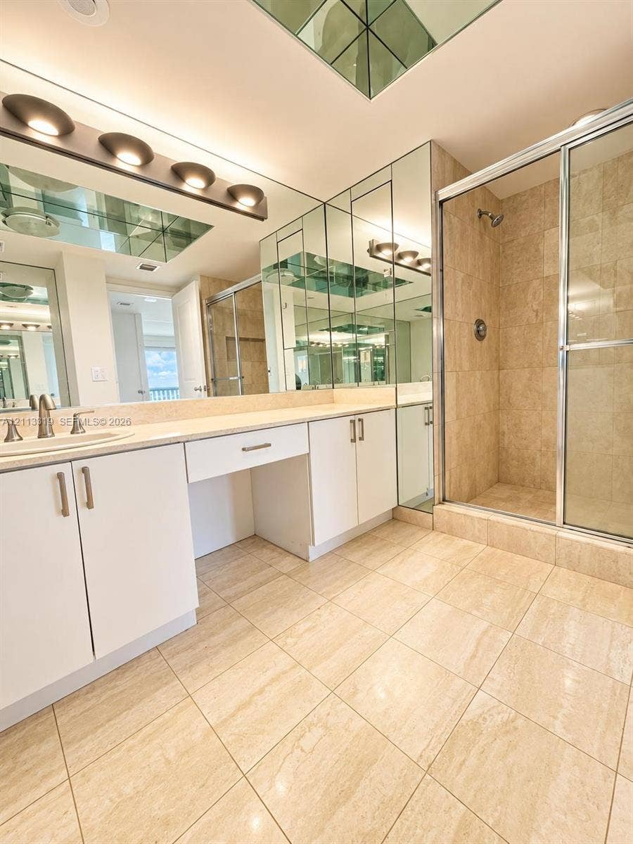 Bathroom featuring a stone-tile floor, wall-to-wall vanity with integrated cabinetry, walk-in shower with metal-framed enclosure, and mirrored wall accents