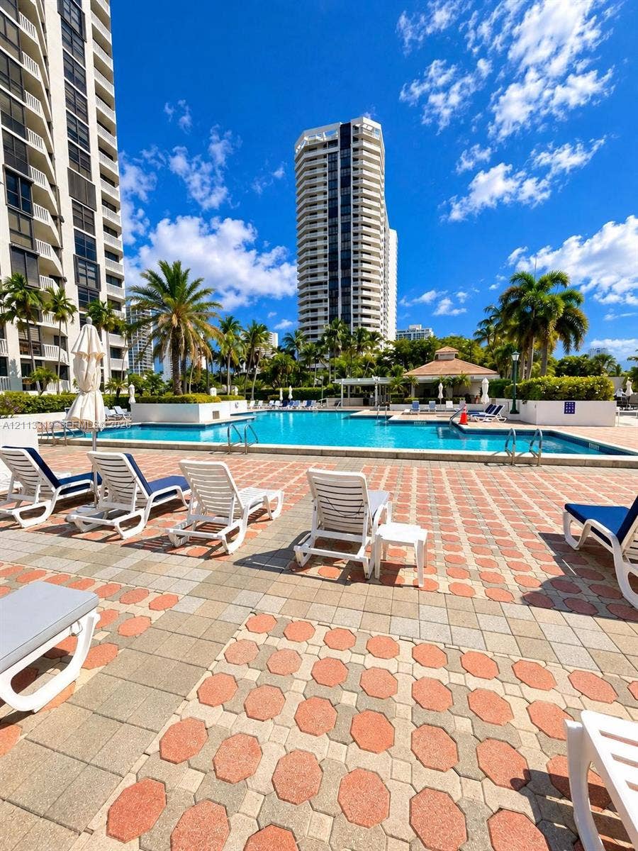 Outdoor swimming pool featuring a paved deck, surrounding mature palm trees, and a shaded pavilion