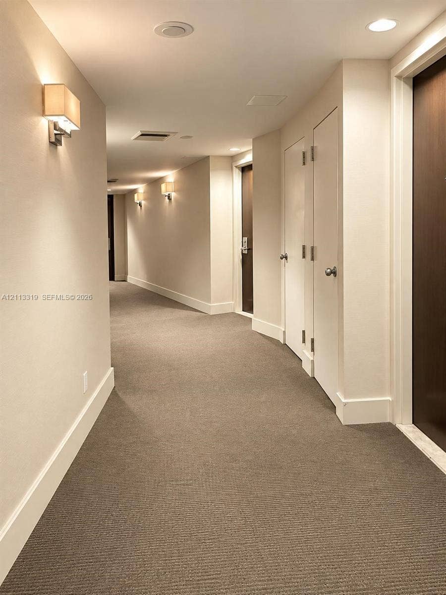 Interior corridor featuring neutral wall-to-wall carpeting, recessed ceiling lighting, wall-mounted sconces, and solid-core interior doors