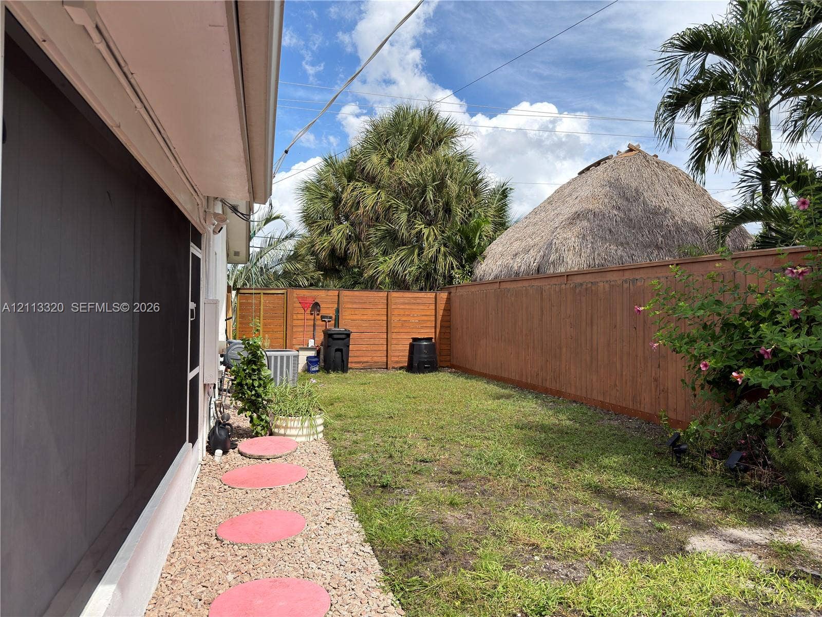 712 NE 25th Avenue, Pompano Beach, FL 33062 Private backyard featuring a horizontal wood-slat perimeter fence, gravel pathway with circular concrete pavers, and mature palm trees