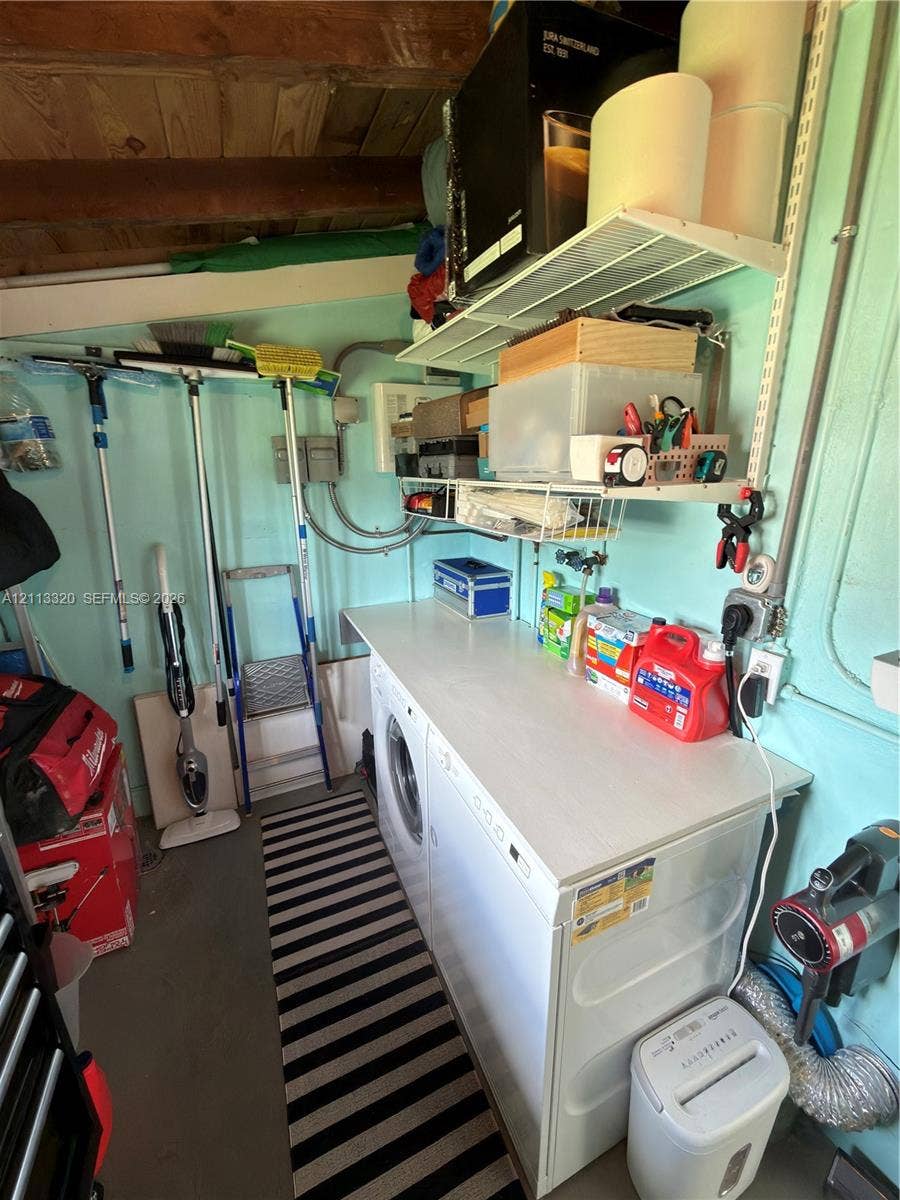 712 NE 25th Avenue, Pompano Beach, FL 33062 Utility area featuring integrated laundry appliances with a flat work surface, adjustable wire wall shelving, exposed wood ceiling beams, and concrete flooring