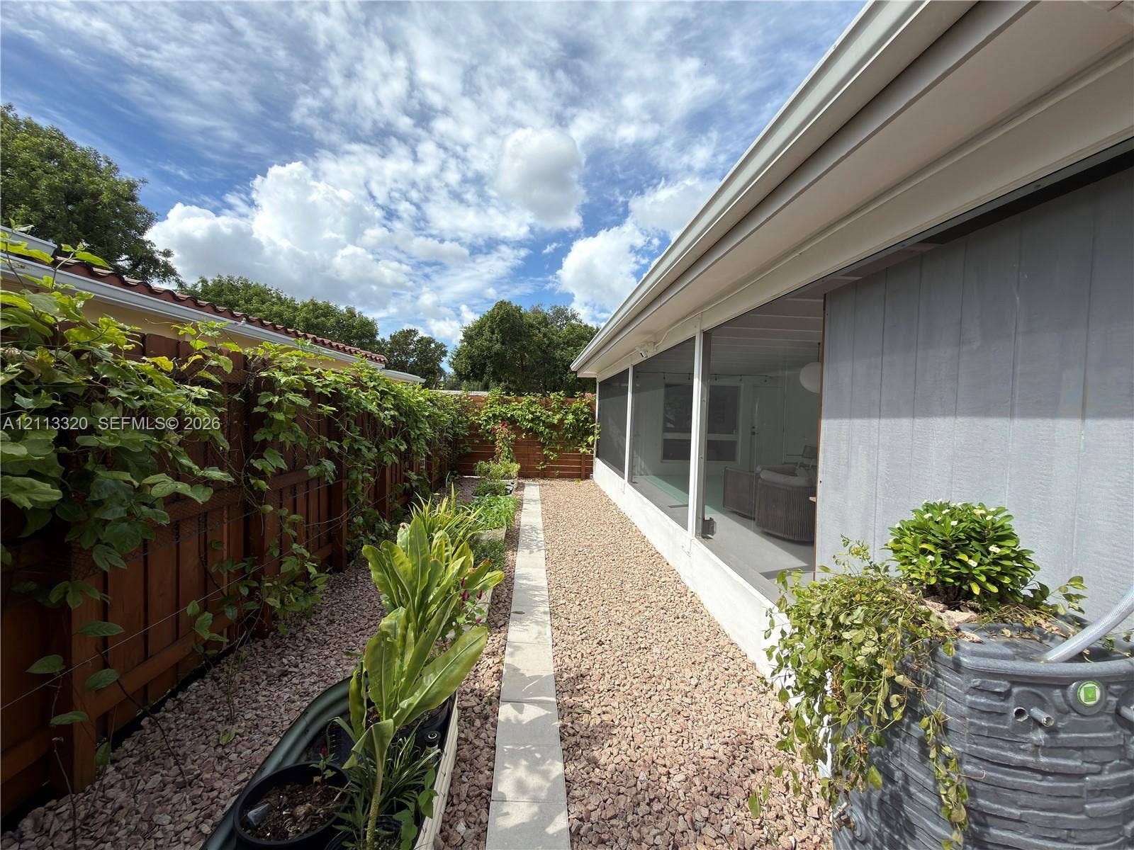 712 NE 25th Avenue, Pompano Beach, FL 33062 Screened-in porch featuring a wood privacy fence, gravel ground cover, raised metal planter beds, and a built-in rainwater collection system
