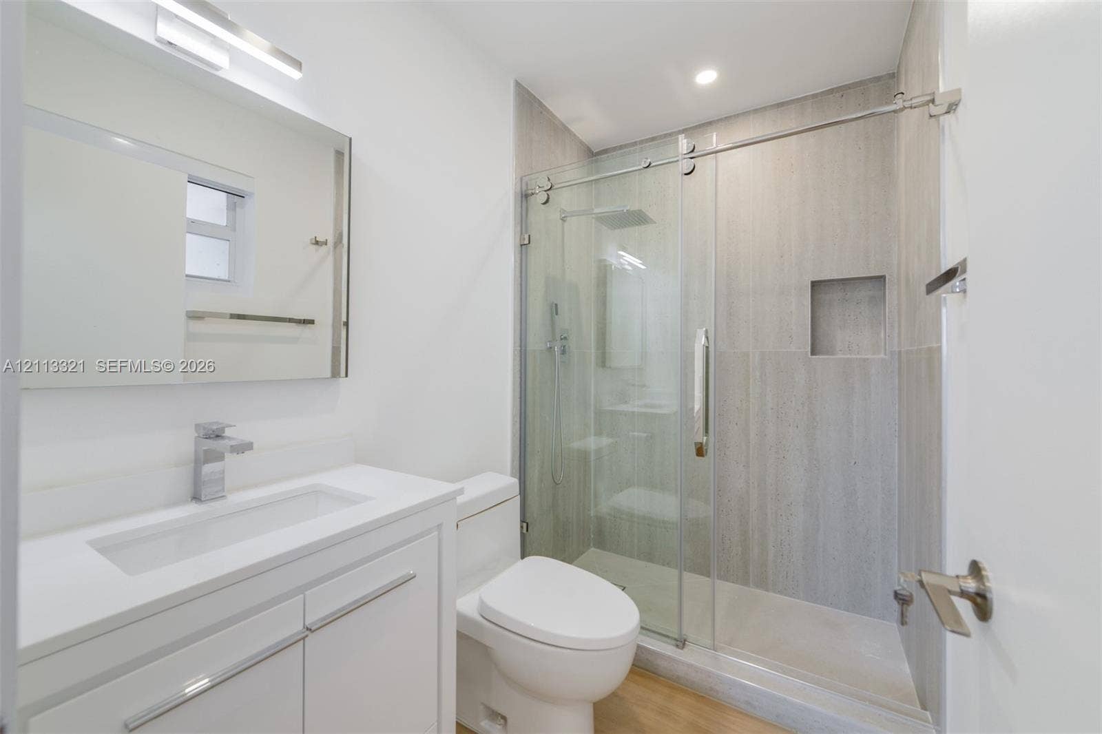 Bathroom featuring a white vanity with a countertop basin, a frameless glass shower enclosure with sliding doors, a recessed wall niche, and large-format tile shower surround