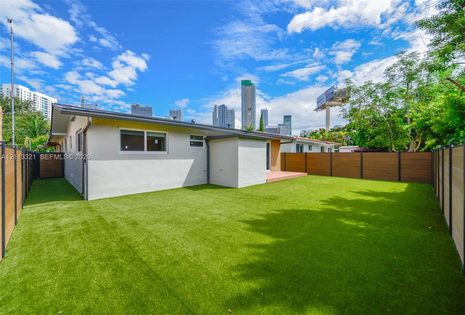 Rear exterior featuring synthetic turf lawn, horizontal wood-finish privacy fencing, and a concrete patio