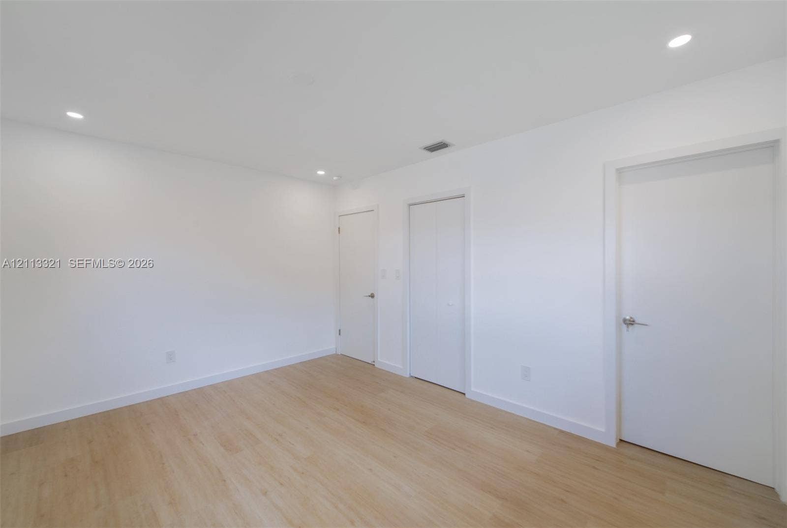Neutral-toned space featuring wood-finish flooring, recessed lighting, and multiple interior doors with brushed nickel hardware