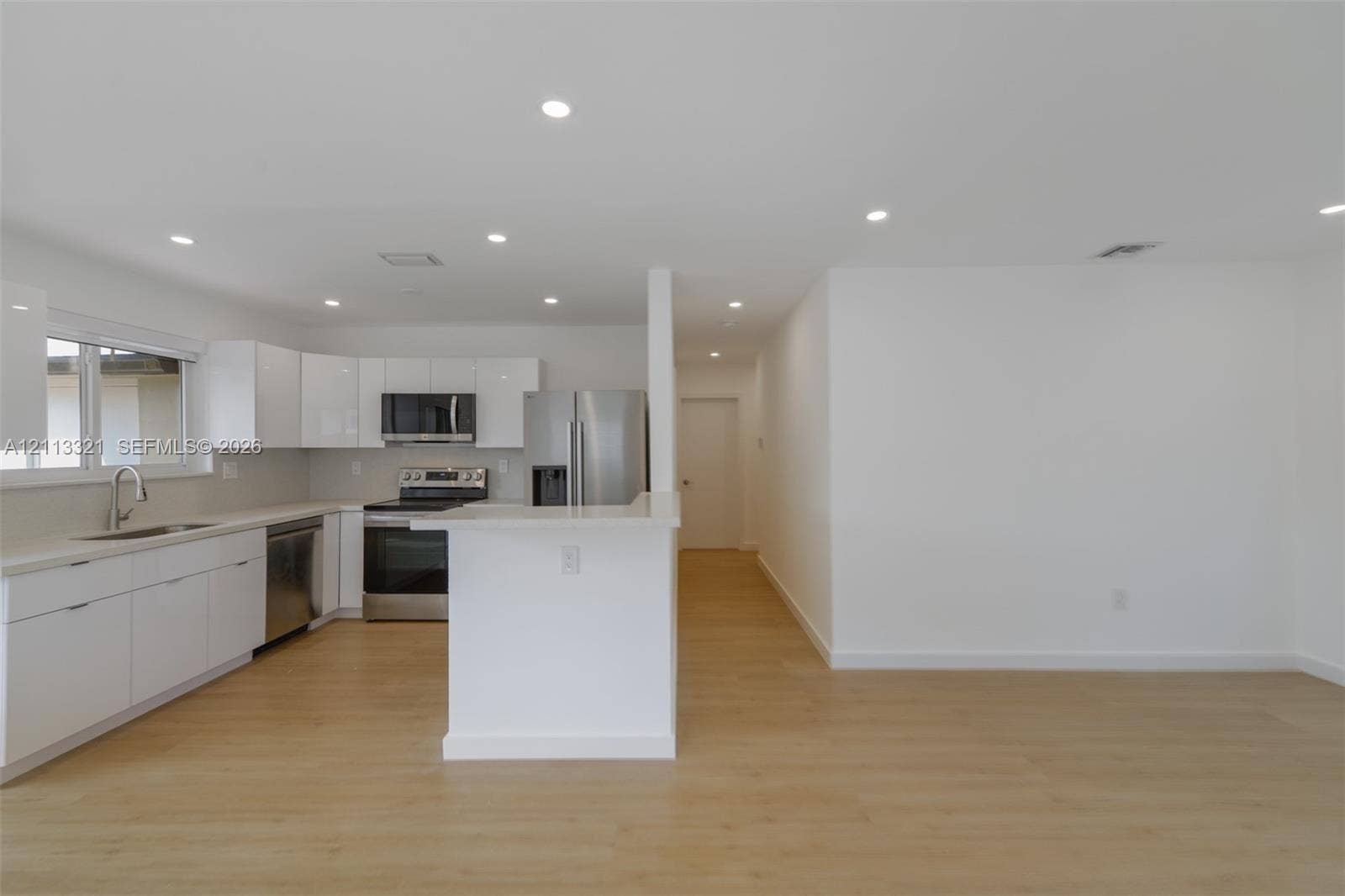 Kitchen featuring white high-gloss cabinetry, stainless steel appliances, a peninsula with stone countertops, and wood-finish flooring illuminated by recessed lighting