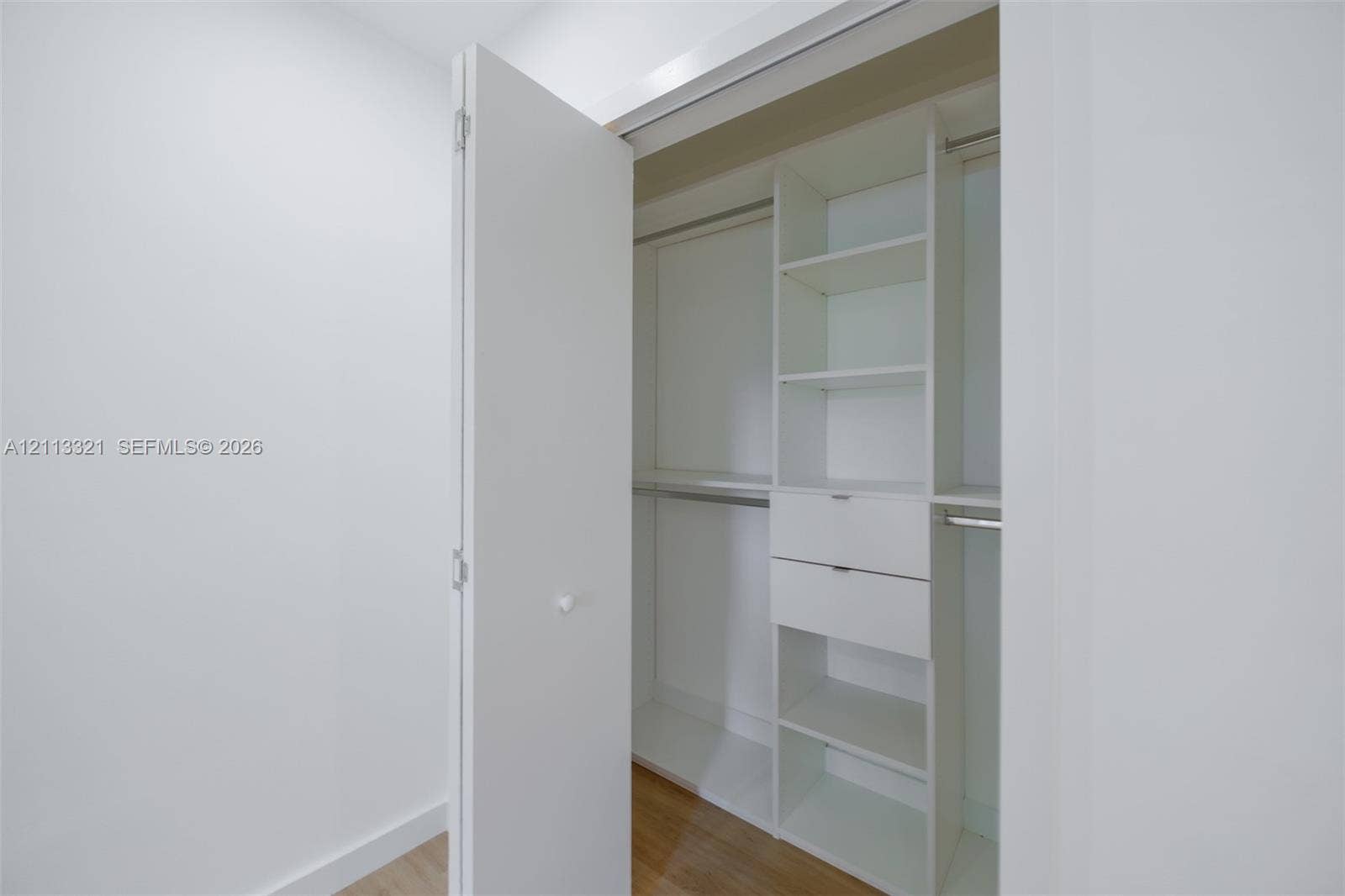 Custom closet featuring white built-in cabinetry, dual drawers, integrated shelving, and metal hanging rods over wood-finish flooring