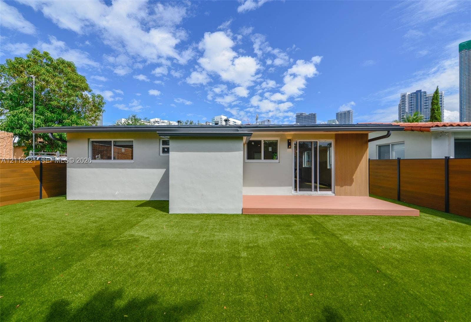 Rear exterior featuring a flat roofline, synthetic turf lawn, solid wood-tone privacy fencing, and a raised ground-level deck
