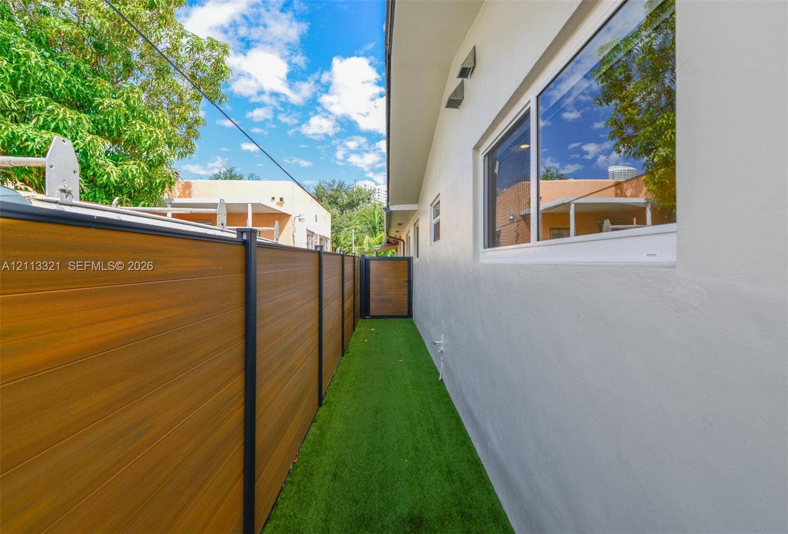 Exterior side yard featuring artificial turf, a horizontal wood-finish privacy fence with metal posts, and smooth-finish stucco siding