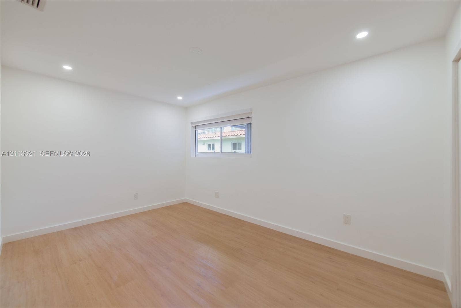 Neutral interior room featuring wood-finish flooring, recessed lighting, and a window with a horizontal blind